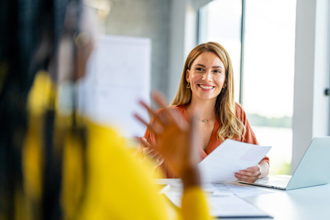Smiling HR professional having a one-on-one meeting in a modern office, holding documents and engaging with a colleague.